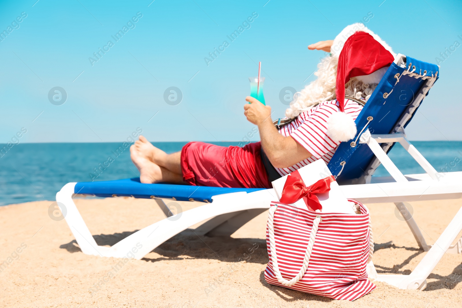 Photo of Authentic Santa Claus with cocktail resting on lounge chair at resort