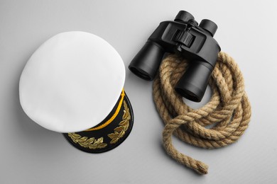 Peaked cap, rope and binoculars on light grey background, flat lay
