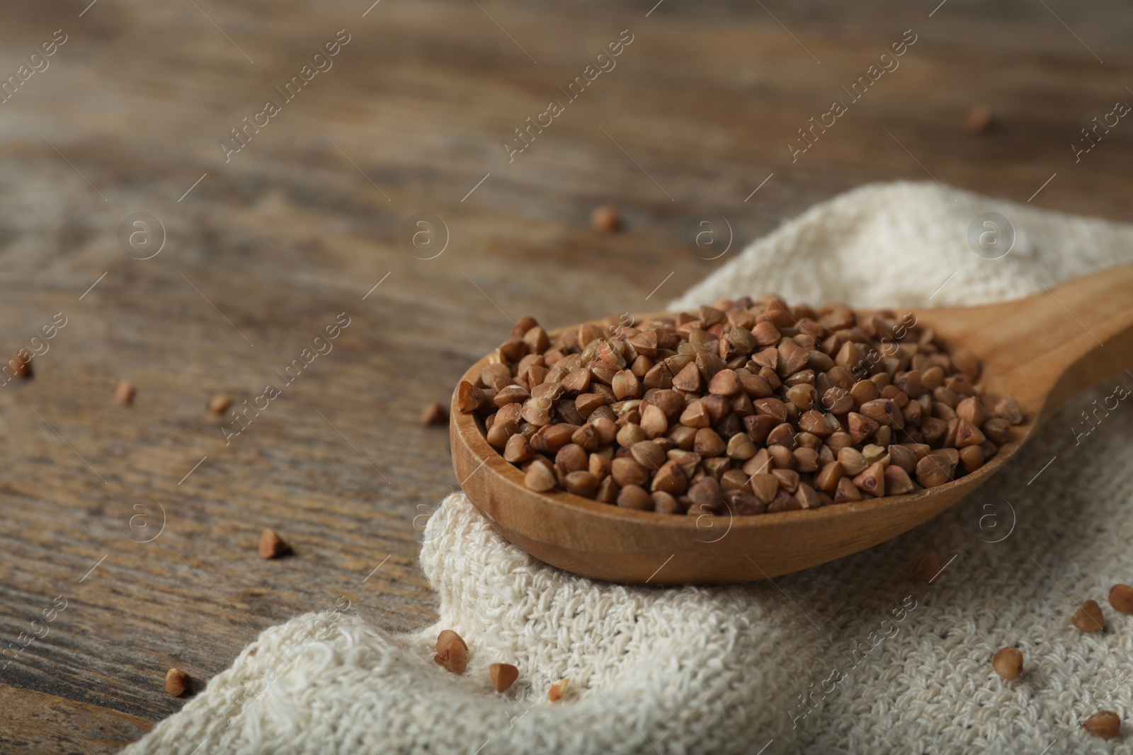 Photo of Spoon with uncooked buckwheat on wooden table. Space for text