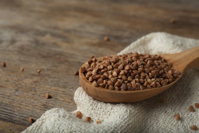 Photo of Spoon with uncooked buckwheat on wooden table. Space for text