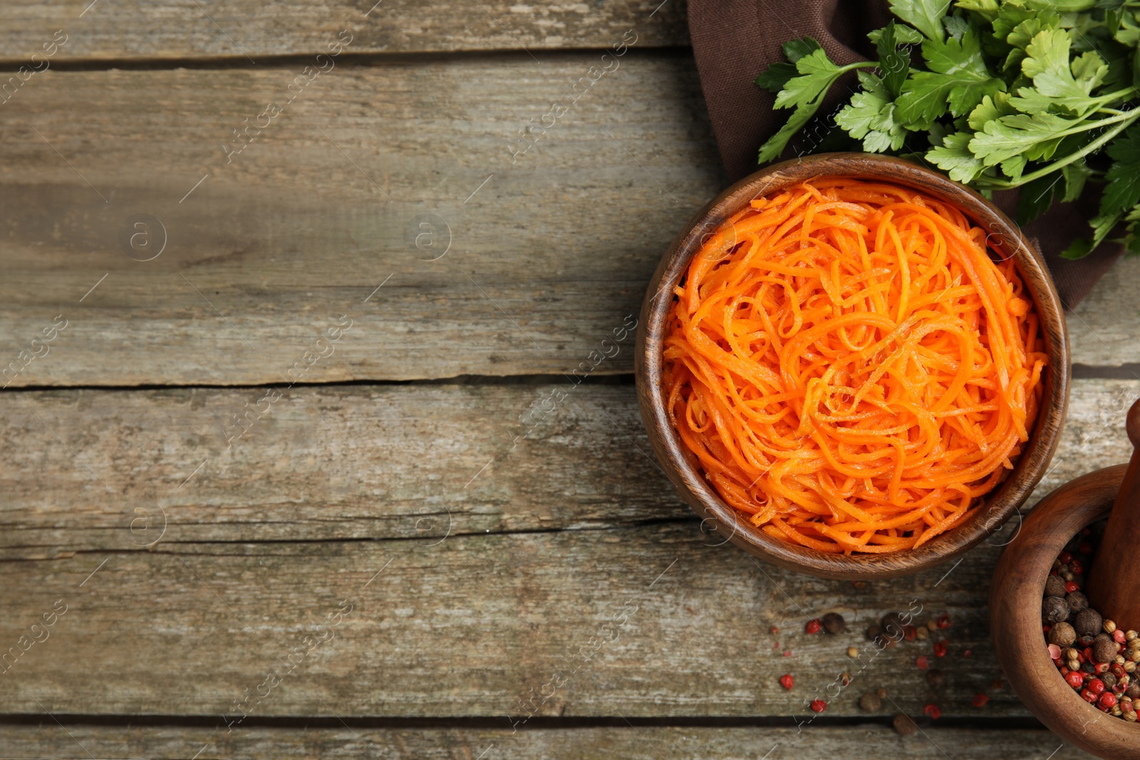 Photo of Delicious Korean carrot salad, parsley and spices on wooden table, flat lay. Space for text