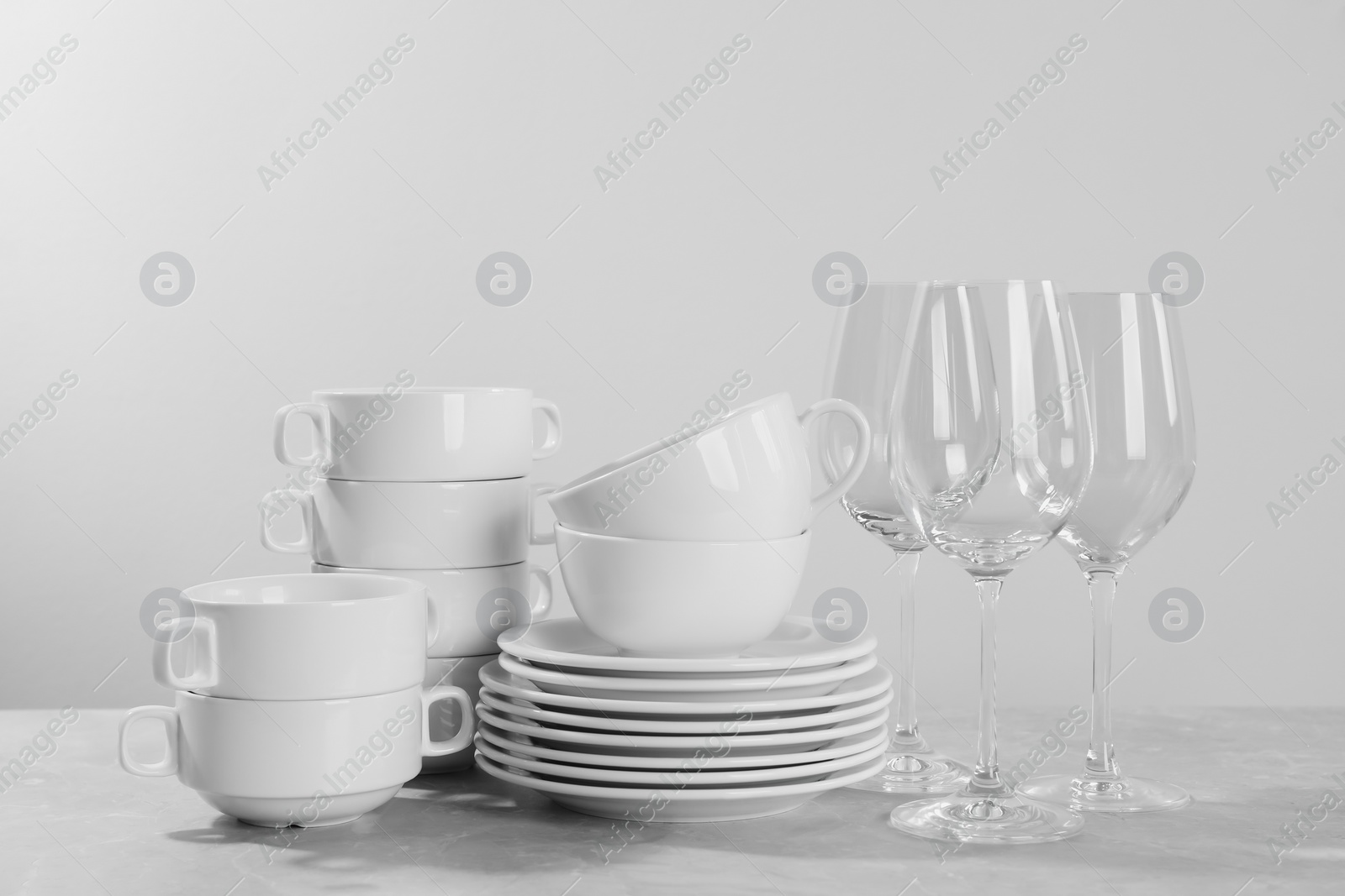 Photo of Set of clean dishware and glasses on grey table against light background