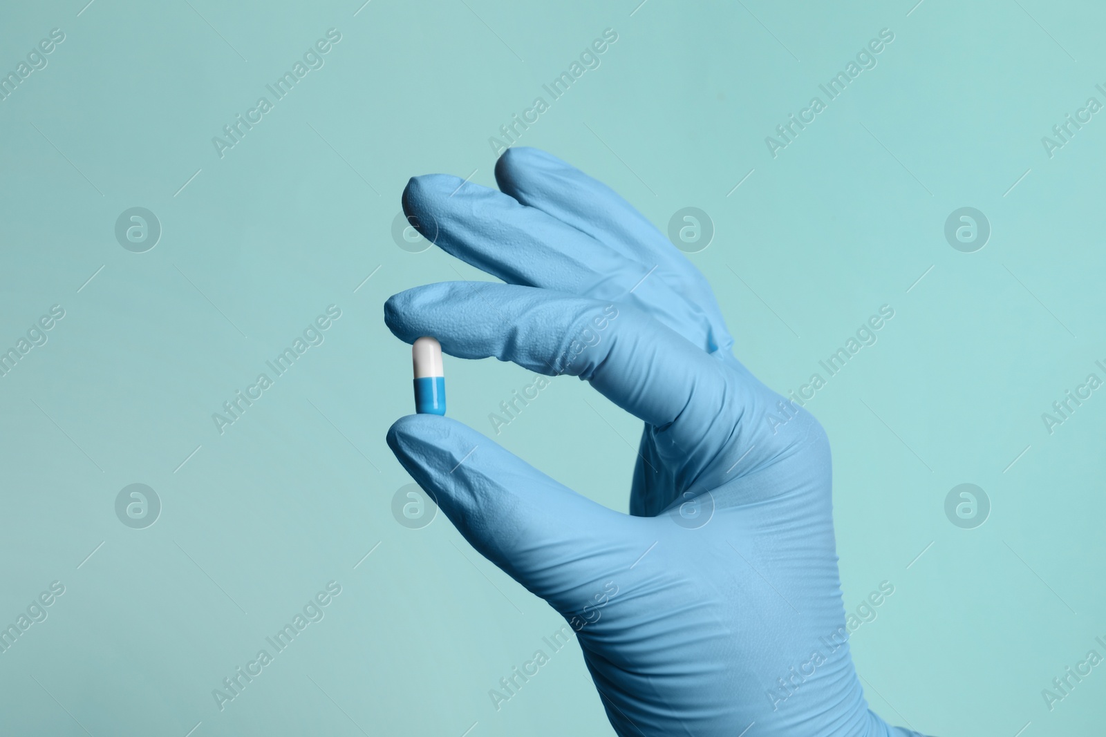 Photo of Doctor holding pill on turquoise background, closeup