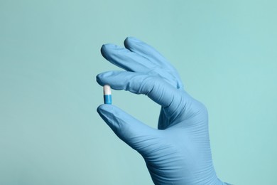 Photo of Doctor holding pill on turquoise background, closeup
