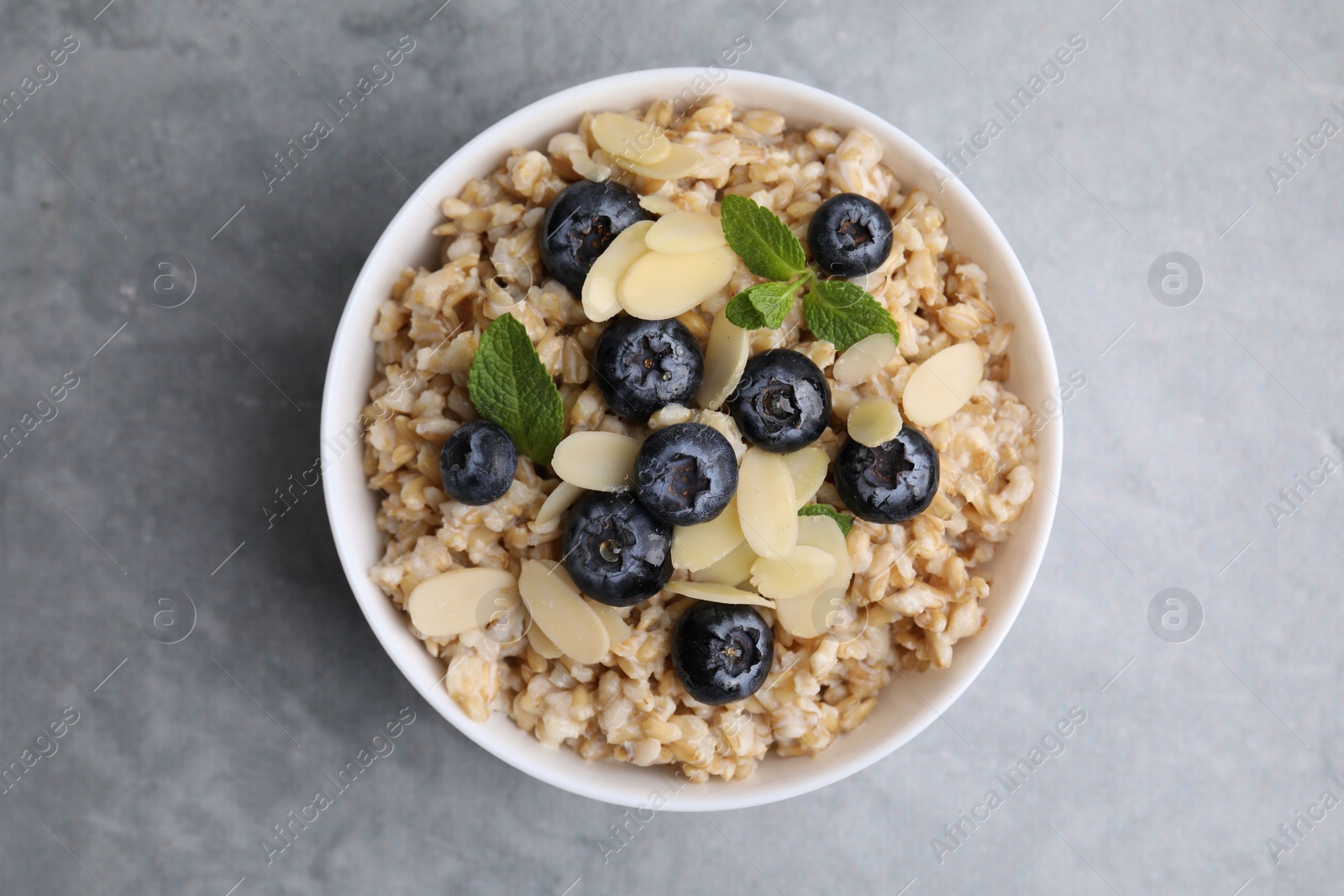 Photo of Tasty oatmeal with blueberries, mint and almond petals in bowl on grey table, top view