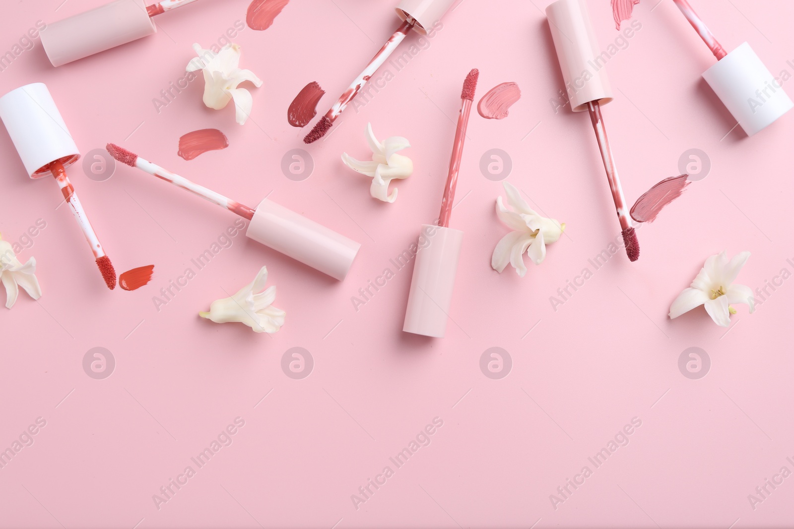 Photo of Different lip glosses, applicators and flowers on pink background, flat lay. Space for text