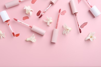 Photo of Different lip glosses, applicators and flowers on pink background, flat lay. Space for text