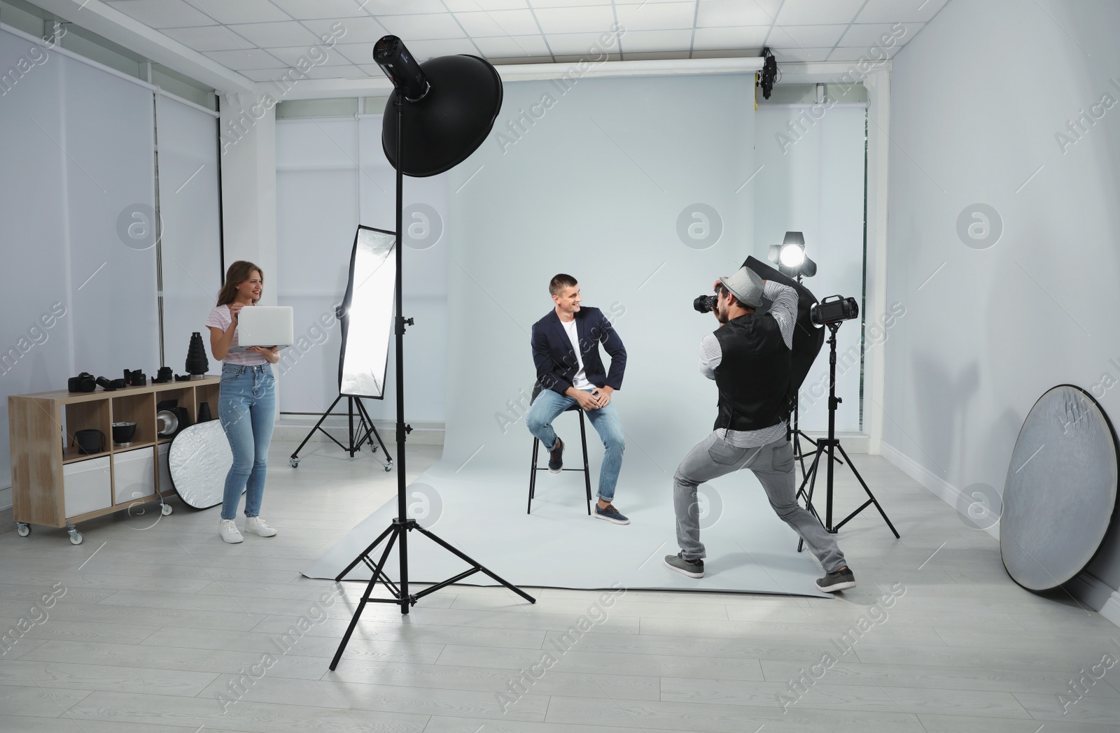 Photo of Professional photographer with assistant taking picture of young man in modern studio