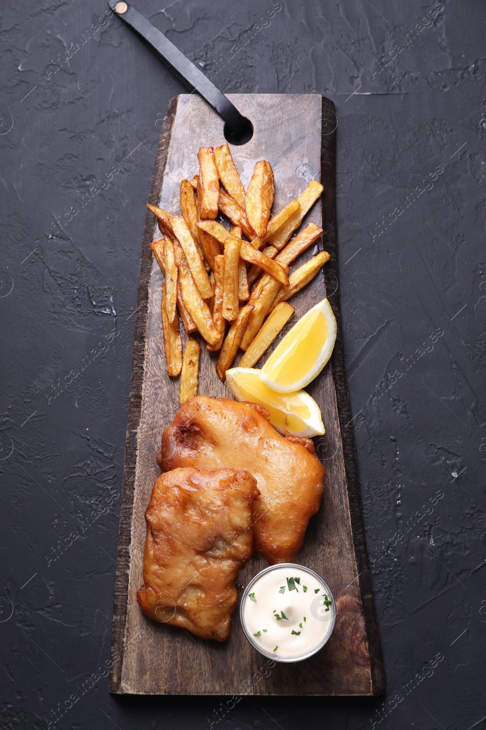 Photo of Tasty fish, chips, lemon and sauce on black table, top view