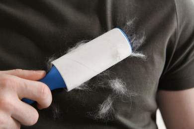 Photo of Man removing hair from grey t-shirt with lint roller, closeup