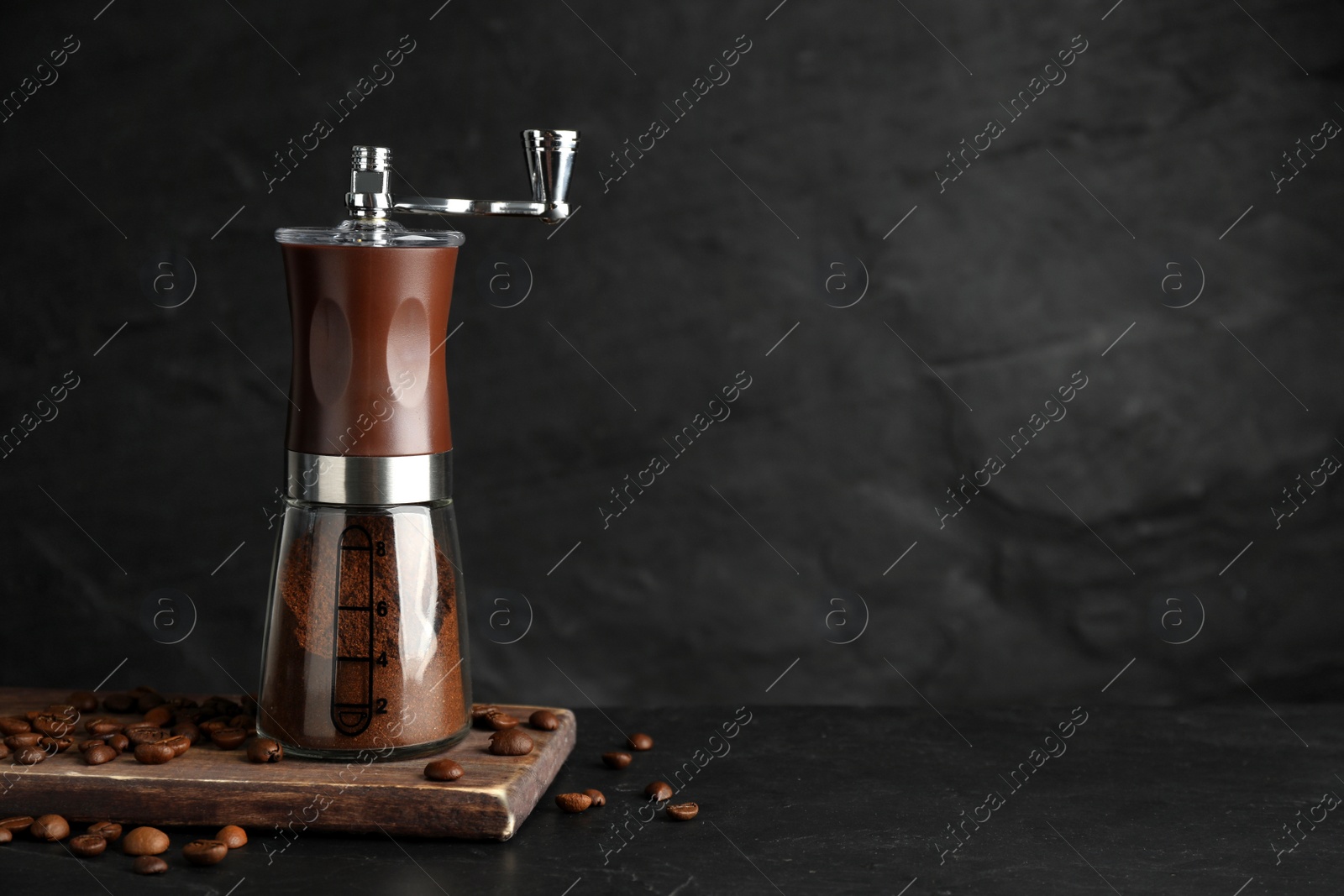 Photo of Manual coffee grinder with powder and beans on black table. Space for text