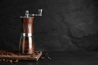 Manual coffee grinder with powder and beans on black table. Space for text