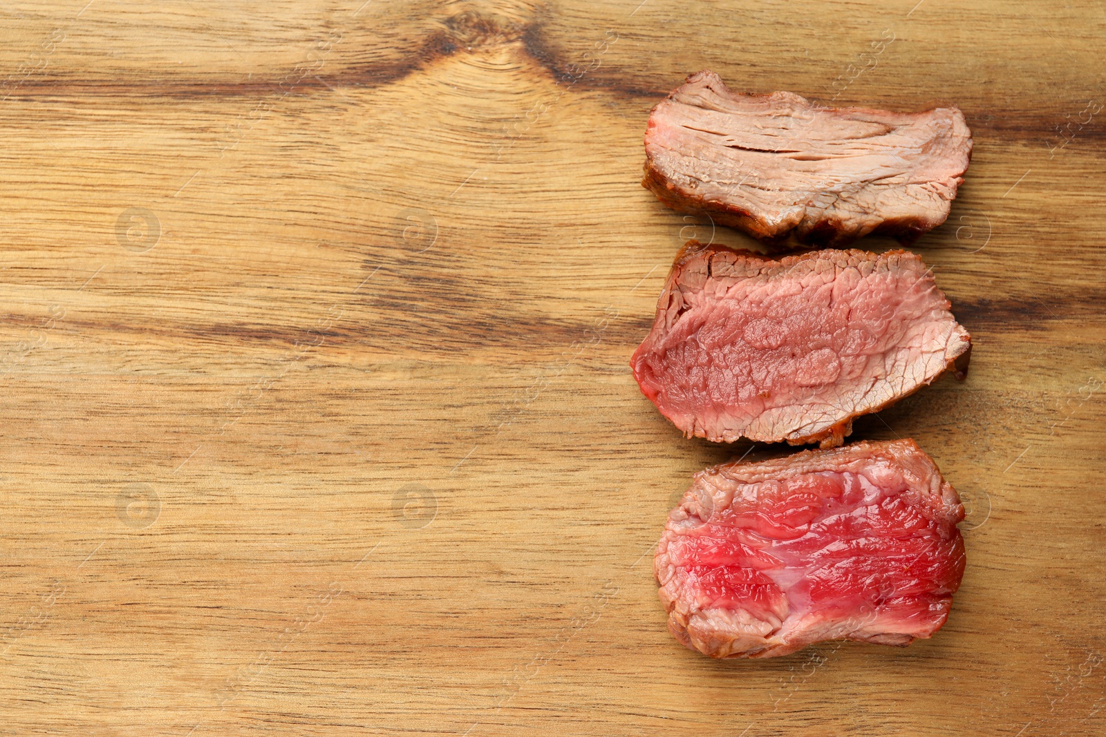 Photo of Delicious sliced beef tenderloin with different degrees of doneness on wooden table, top view. Space for text