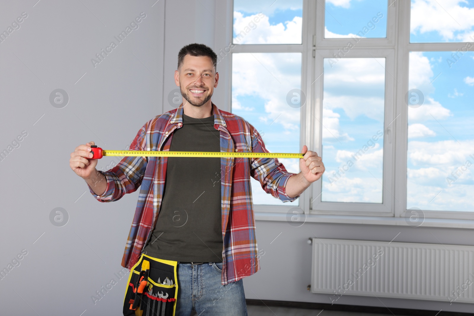Photo of Handsome worker with measuring tape in empty room