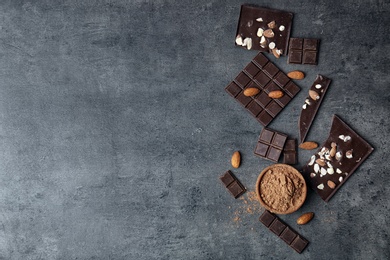 Cocoa powder in bowl and tasty chocolate with nuts on dark table, top view