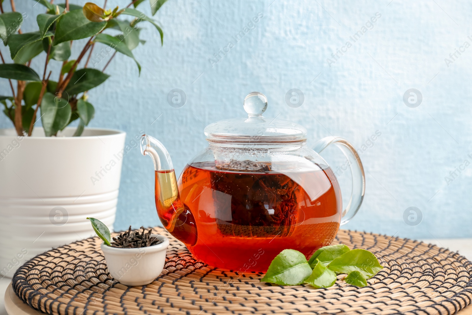 Photo of Teapot with hot aromatic tea, dry and fresh leaves on wicker mat