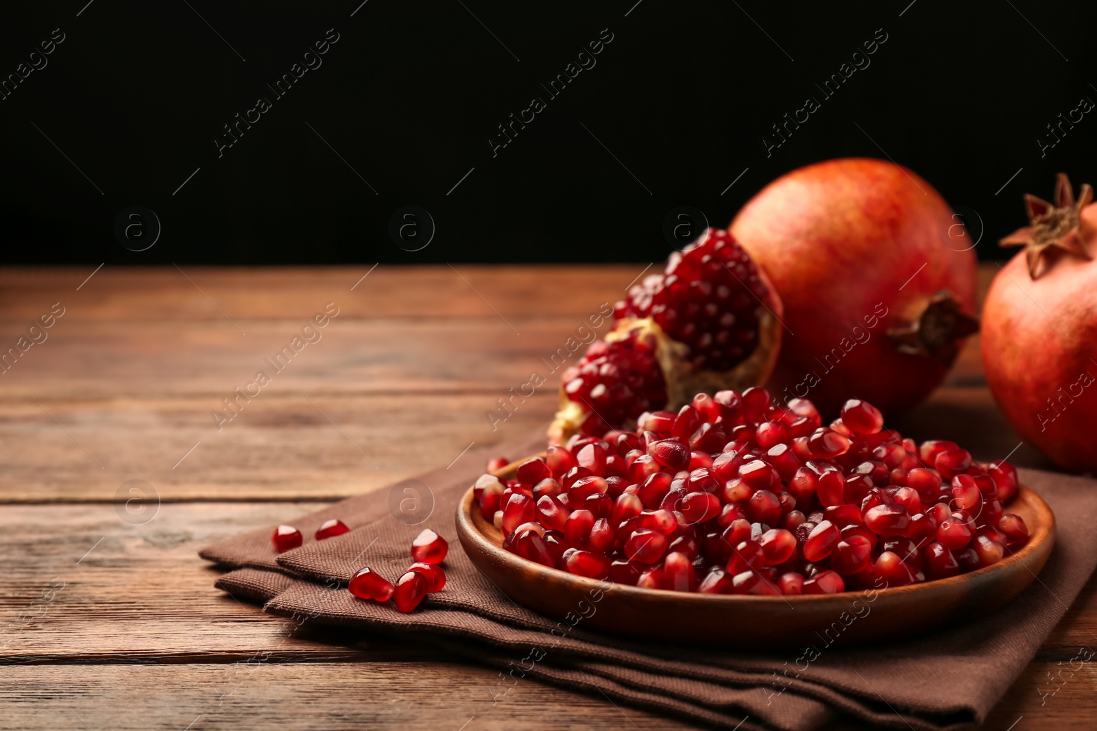 Photo of Ripe juicy pomegranates and grains on wooden table. Space for text