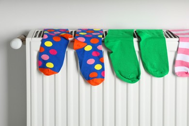 Different colorful socks on heating radiator near white wall