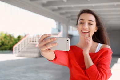 Photo of Attractive young woman taking selfie with phone outdoors