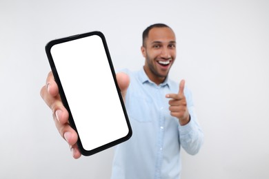 Photo of Young man showing smartphone in hand and pointing at it on white background, selective focus. Mockup for design