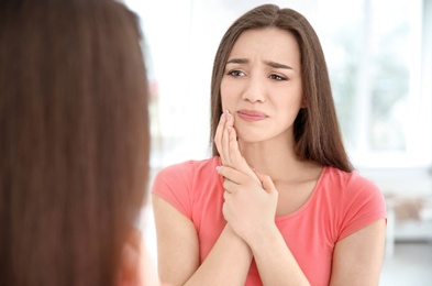 Reflection of woman with sensitive teeth in mirror indoors