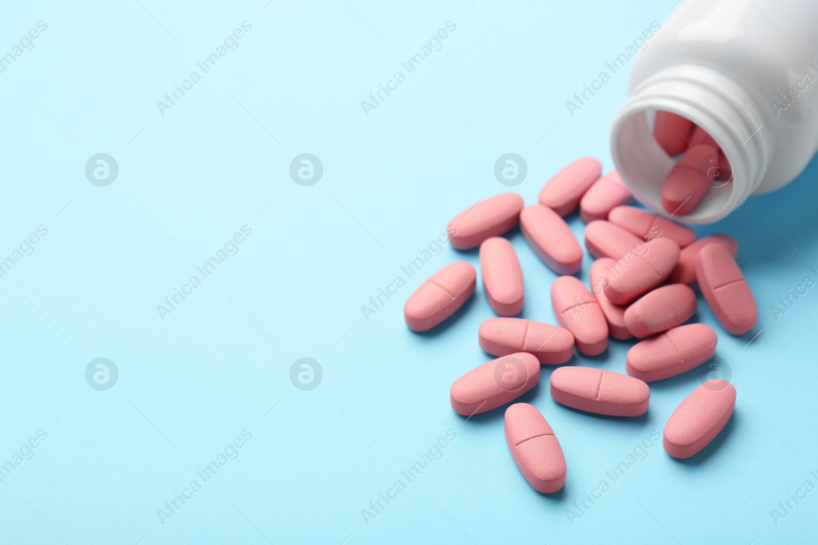 Photo of Vitamin pills and bottle on light blue background, closeup. Space for text