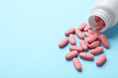 Photo of Vitamin pills and bottle on light blue background, closeup. Space for text