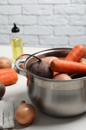 Photo of Pot with fresh vegetables on white wooden table. Cooking vinaigrette salad