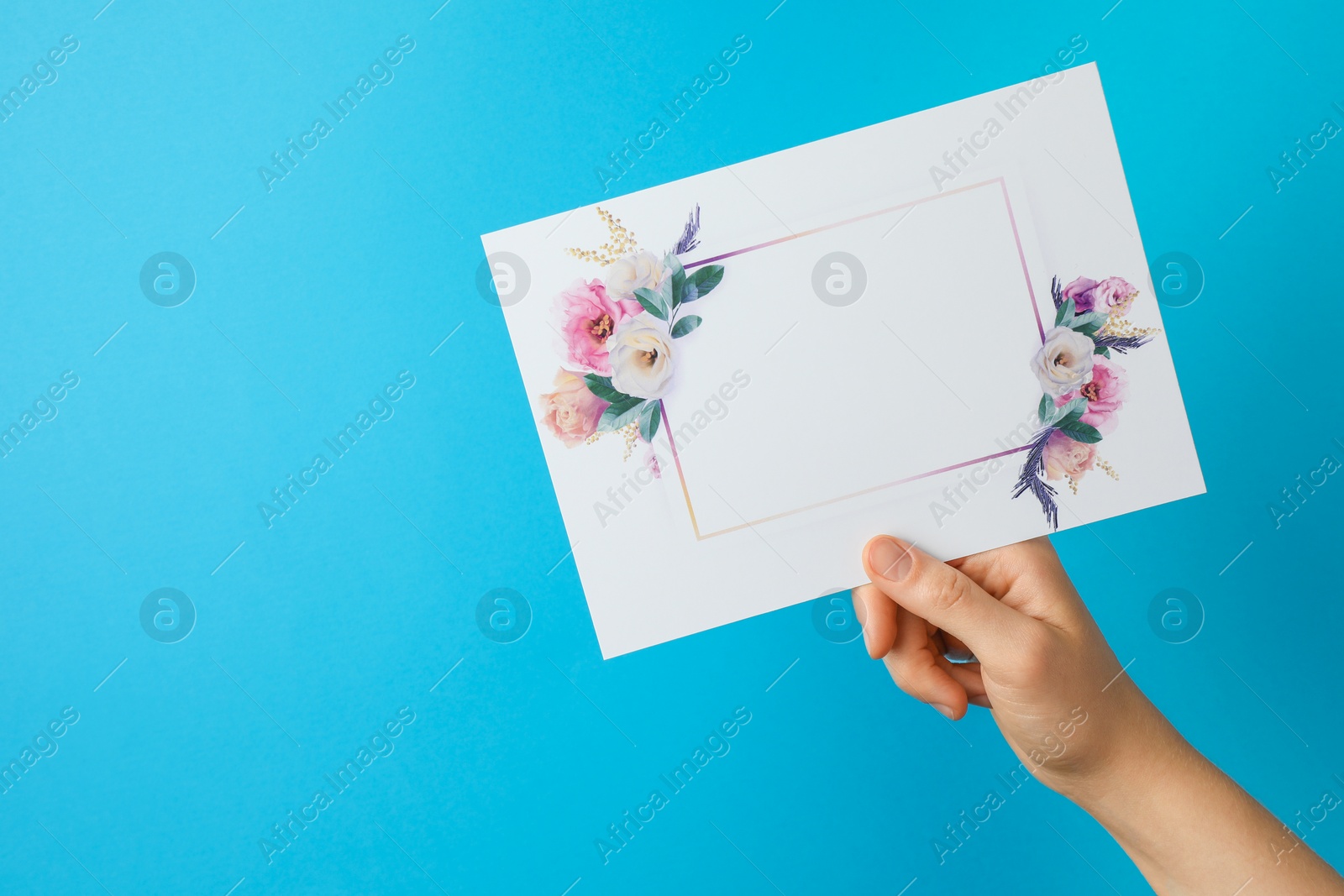 Photo of Woman holding blank invitation card on light blue background, closeup. Space for text