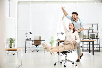 Photo of Office employee giving his colleague ride in chair at workplace. Space for text