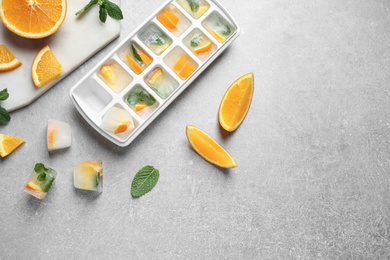 Photo of Ice cubes in tray with orange slices and mint on light grey table, flat lay