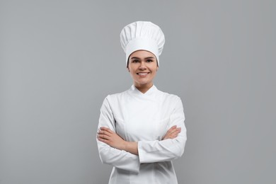 Happy female chef wearing uniform and cap on light grey background
