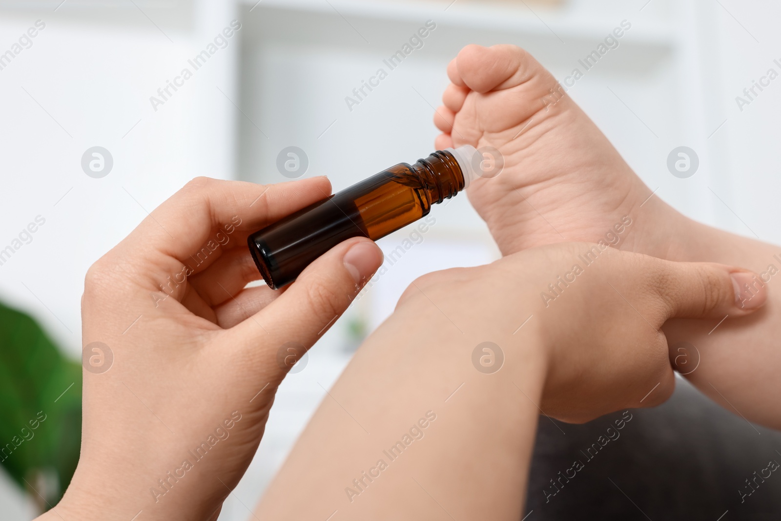 Photo of Mother applying essential oil from roller bottle onto her baby`s heel indoors, closeup