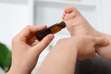 Mother applying essential oil from roller bottle onto her baby`s heel indoors, closeup