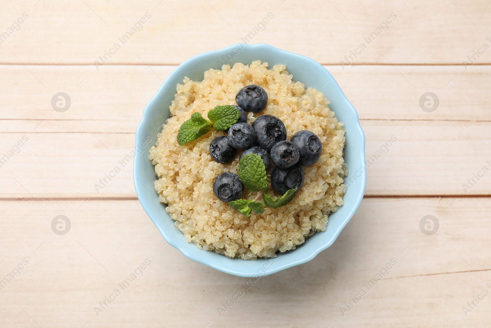 Photo of Tasty quinoa porridge with blueberries and mint in bowl on light wooden table, top view