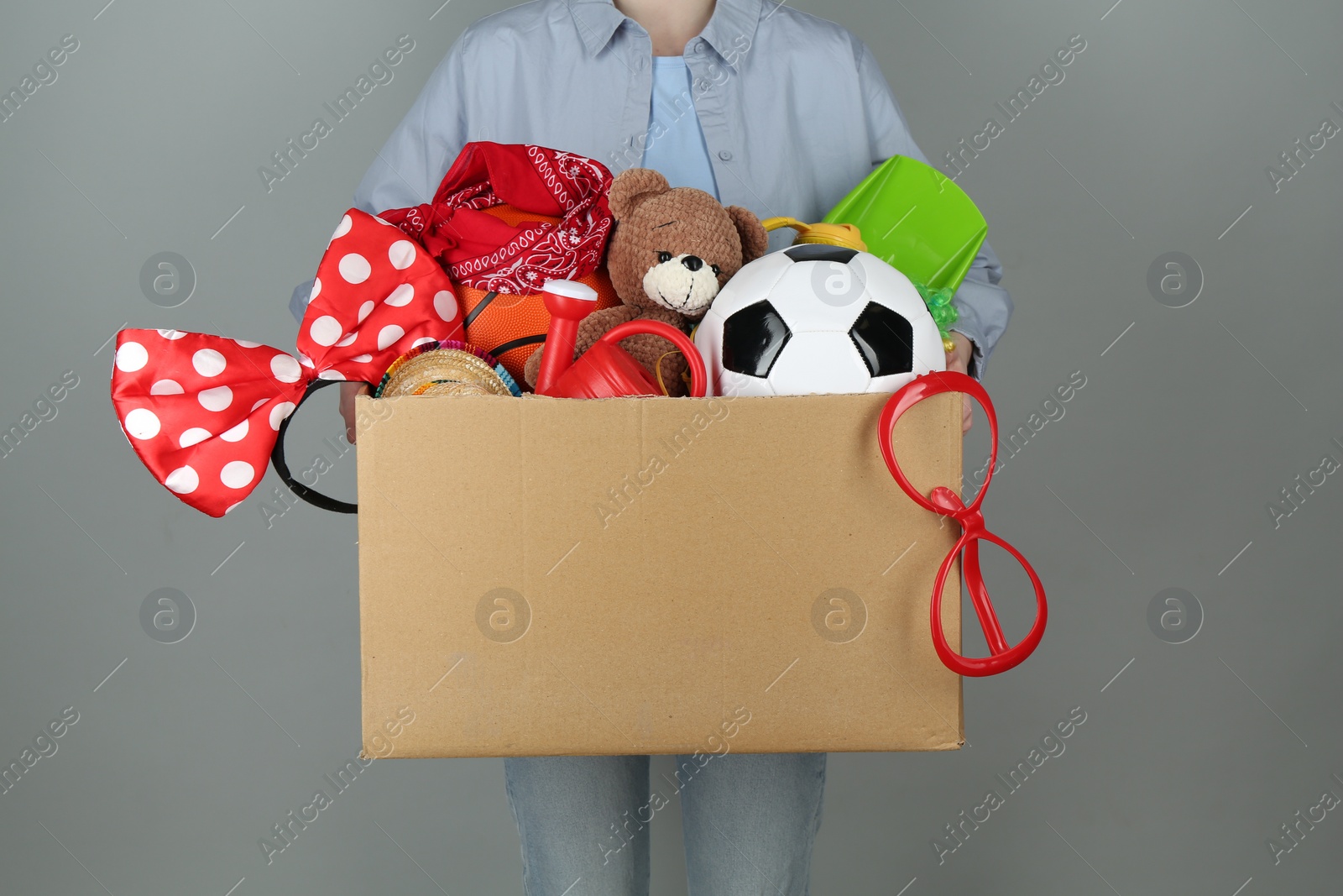 Photo of Woman holding box of unwanted stuff on grey background, closeup