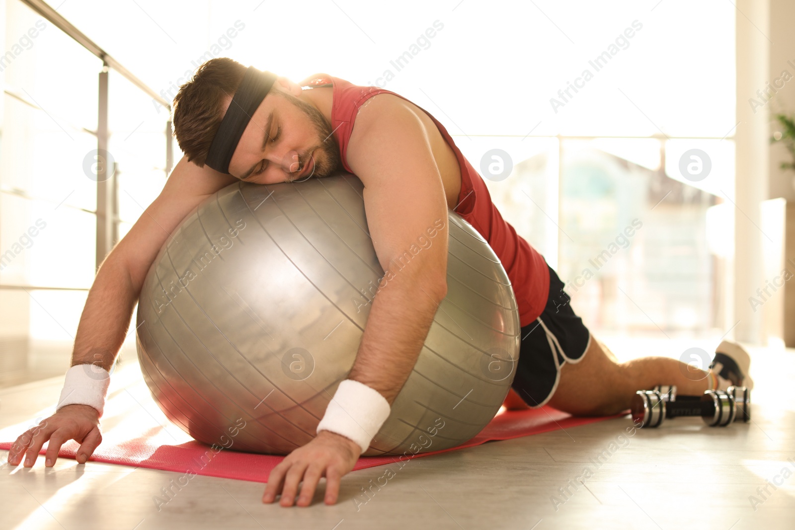 Photo of Lazy young man with exercise ball on yoga mat indoors