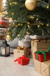Gift boxes under Christmas tree and lantern with candle indoors