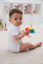 Photo of Cute baby boy playing with toy on floor at home