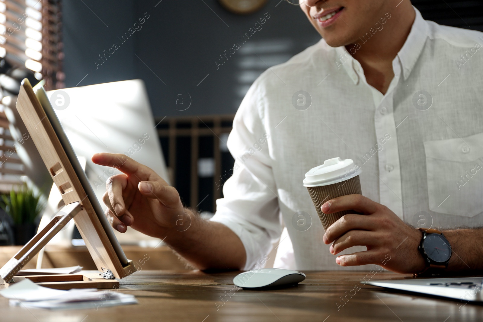 Photo of Freelancer with cup of coffee working on tablet at table indoors, closeup