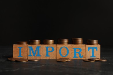 Photo of Word Import made of wooden cubes with letters and coins on black table