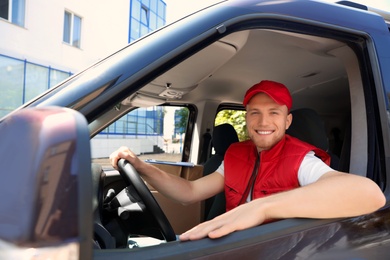 Photo of Young courier with parcels in delivery car