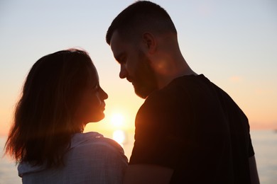 Happy young couple together near sea at sunset