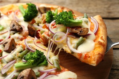 Photo of Taking piece of delicious vegetarian pizza at wooden table, closeup
