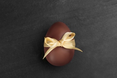 Photo of Sweet chocolate egg with beige bow on black table, top view