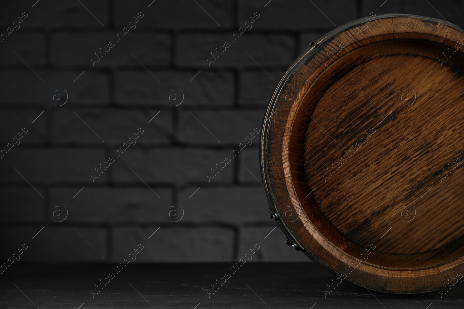 Photo of One wooden barrel on table near brick wall, closeup. Space for text