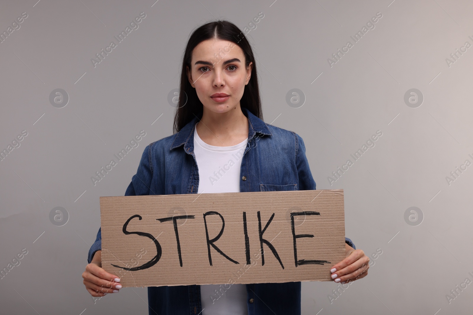 Photo of Woman holding cardboard banner with word Strike on grey background