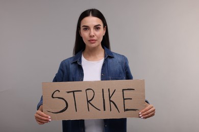 Woman holding cardboard banner with word Strike on grey background