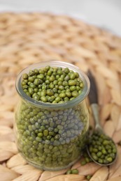 Photo of Glass jar of mung beans with spoon on wicker mat, closeup