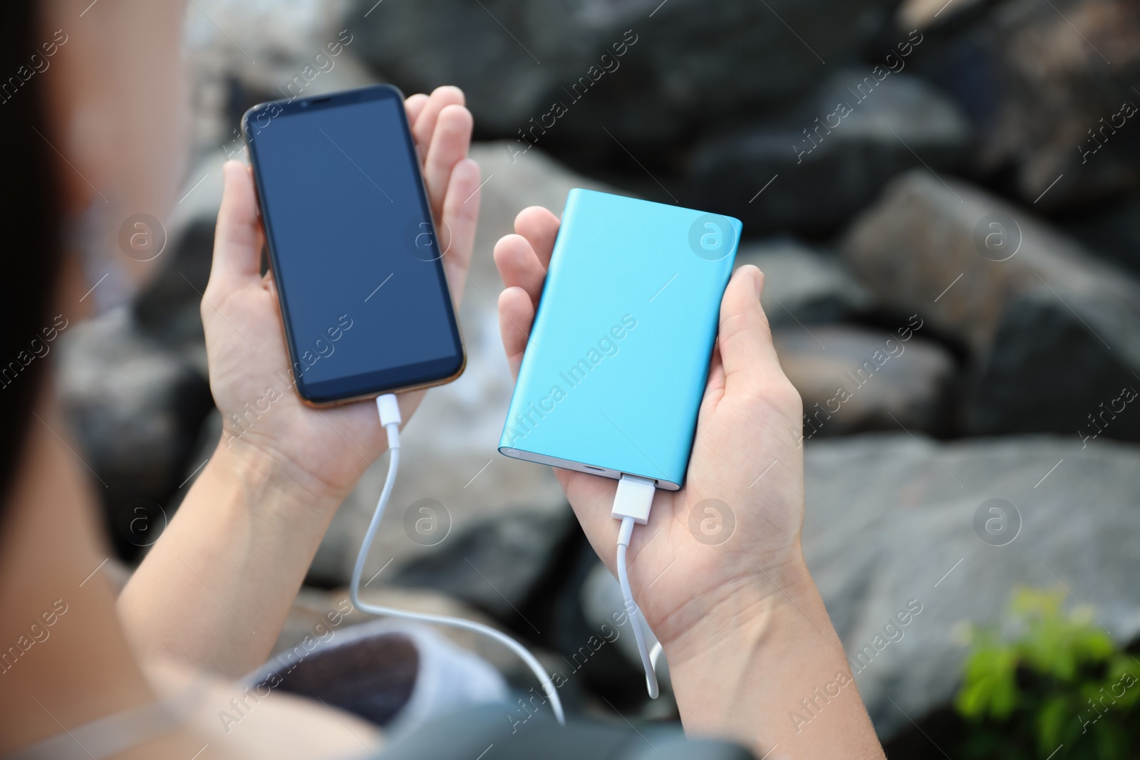 Photo of Woman charging smartphone with power bank on rocky mountain, closeup